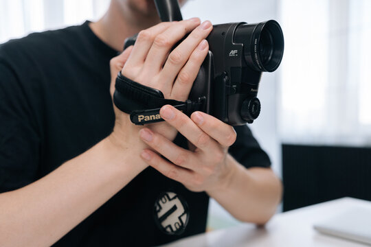 Close-up shot of male hands holding vintage camcorder. Person in black shirt films with retro equipment. Concept of nostalgia, old technology, filmmaking, vlogging content creation. Bright lighting.