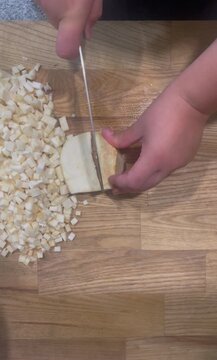 Top-down footage of a cook using a sharp stainless steel knife to finely slice and dice celeriac root on a wooden cutting board.