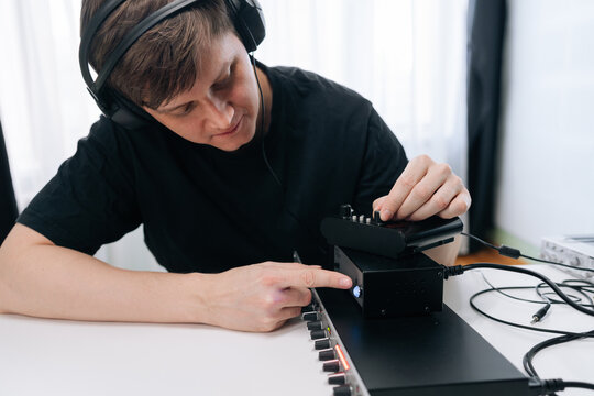 Man in headphones focused on adjusting professional audio equipment. Sound engineer or music producer working at mixing console in bright, minimalist studio. Close-up on hands and controls.