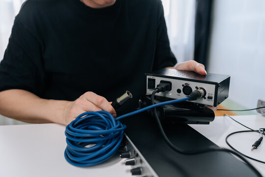 Close-up of sound engineer connecting microphone cable to audio preamp. Professional recording studio setting with equipment on white table. Focus on technical setup and connectivity.