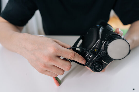 Close-up of hands plugging cable into retro camcorder. Person prepares old video equipment on white table. Nostalgia concept for filmmaking and vintage technology. Bright, clean background.