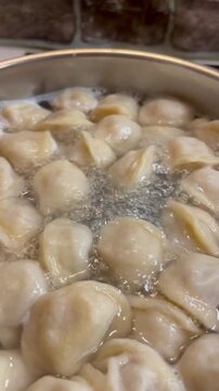 Close-up video of traditional meat dumplings pelmeni boiling in bubbling hot water inside a metal pot on an induction stove during cooking.