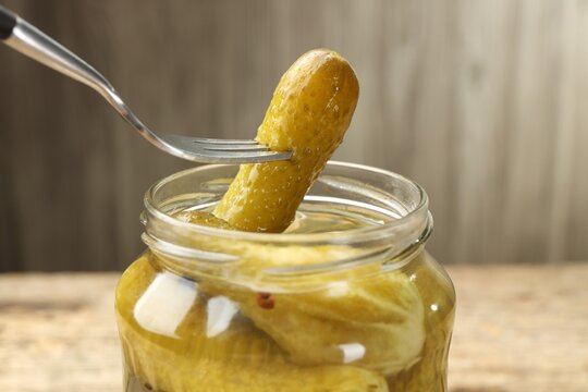 Taking pickled cucumber from glass jar at table, closeup