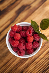 Fresh raspberries in a white bowl on a wooden table © Kateryna
