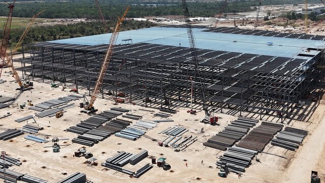 Aerial views of commercial building under construction with steel framing, surrounded by tower cranes