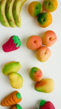 Vertical video of camera panning right over colorful marzipan fruits on white background