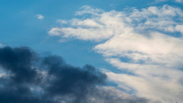 A dark cloud bank meets pale wisps across open blue sky 