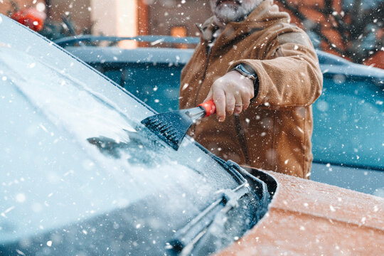 Man clears snow from car windshield on a winter day in the city