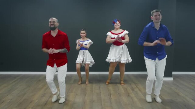 Dance instructors guide couples through bachata steps in modern studio space with stationary camera capturing interactive instruction, rhythmic movement, colorful costumes.