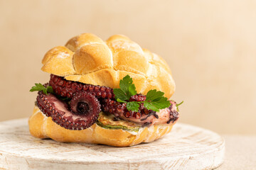 Italian sandwich made with traditional tartaruga bread, filled with stracciatella cheese, grilled zucchini, tender octopus tentacles and fresh parsley,  on a light beige background. © Olga