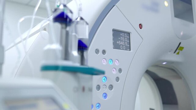 Automatic contrast injector in close-up with a modern CT scanner blurred in the background.