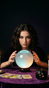 Woman gazing into crystal ball beside tarot cards at Halloween fortune-telling table. Tarot reading and divination practice. Halloween portrait for seasonal occult entertainment