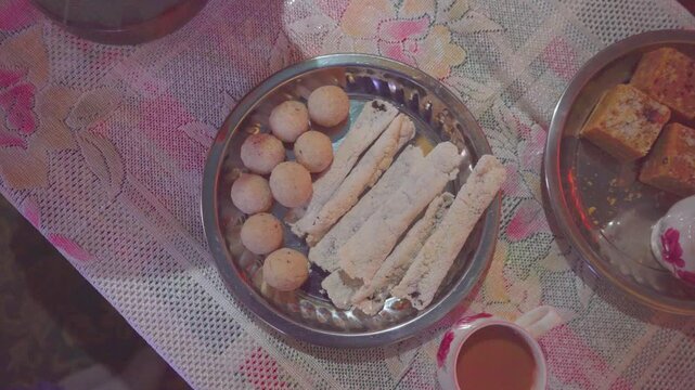 Traditional Assamese sweets Til Pitha made with jaggery and coconut Laru served on decorative table with tea in Assam, India.