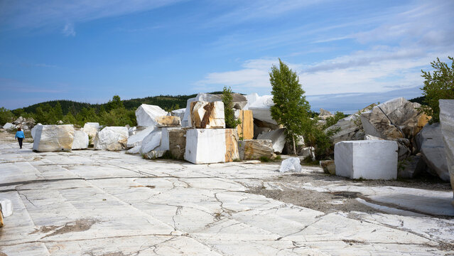 Large white marble blocks in a stone quarry. Wide landscape view of raw material extraction in summer. Industrial mining of natural resources under a blue sky