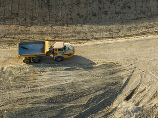 Aerial view of a yellow dump truck driving along a dirt road at a construction site in early morning light. © Mario