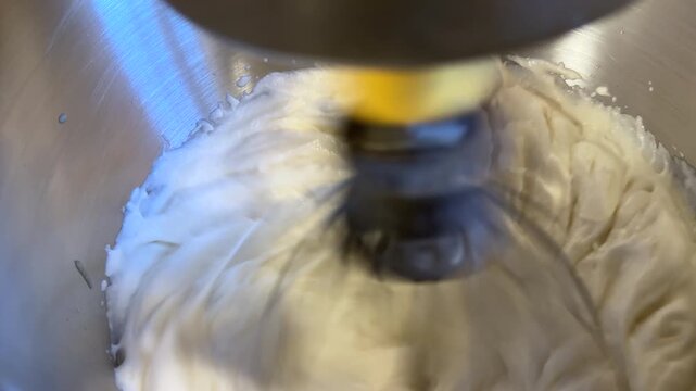 Close up of a white fluffy mixture being whisked at fast speed in a stand mixer bowl 