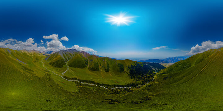 360-degree aerial panorama captures vast mountainous landscape in Kyrgyzstan. Rolling green hills lead to steep slopes, with a winding river and dense forest visible in the distance.