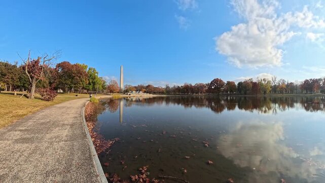  Washington Monument reflects beyond a curving waterside path in this autumn 4K video.
