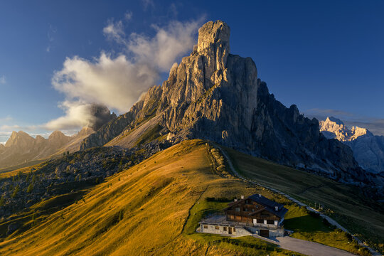  Golden hour view of Ra Gusela rising above grassy alpine slopes and a mountain hut at Passo Giau in the Dolomites, Italy, supporting themes of hiking, mountain travel and outdoor recreation.