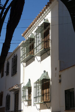 Traditional white house facade featuring ornate wrought iron balconies and terracotta roof tiles under a bright blue sky, capturing classic Spanish architecture