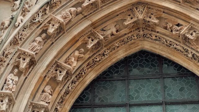 Tilt up shot of an ornate Gothic cathedral entrance featuring intricate stone carvings, statues of saints, and an open red portal revealing the historic interior with stained glass.

