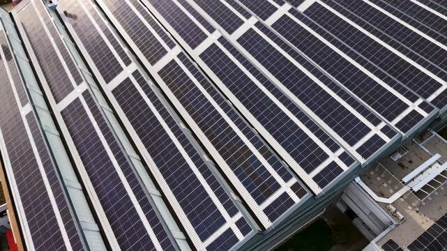 4k Aerial view solar panel facade on modern high rise with bright sun flare, glass and metal surfaces, strong geometric lines, clean energy architecture