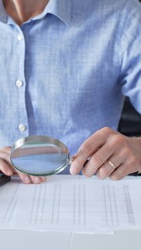 Adult male accountant analyzing financial documents, using magnifying glass and calculator at workplace desk, focused on detailed accounting review, close up. Audit and taxes in business