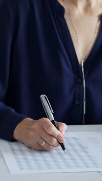 Businesswoman or accountant is sitting at desk using calculator and taking notes, with laptop nearby, performing accounting and financial analysis tasks, close up. Audit and taxes theme in business