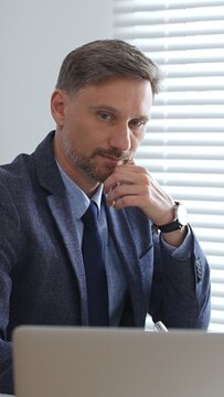 Professional businessman working at office desk, analyzing financial documents using laptop and calculator while wearing tailored suit. Audit and taxes in business