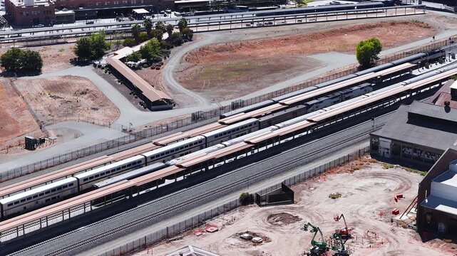 Aerial view looking down at passenger trains parked along platforms at the Sacramento Valley Station rail yard, surrounded by tracks, maintenance areas, and industrial structures in California.