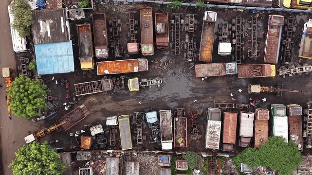 Aerial view of a truck scrapyard with rows of parked vehicles and rusted trailers on muddy ground in Chennai, Tamil Nadu, India.