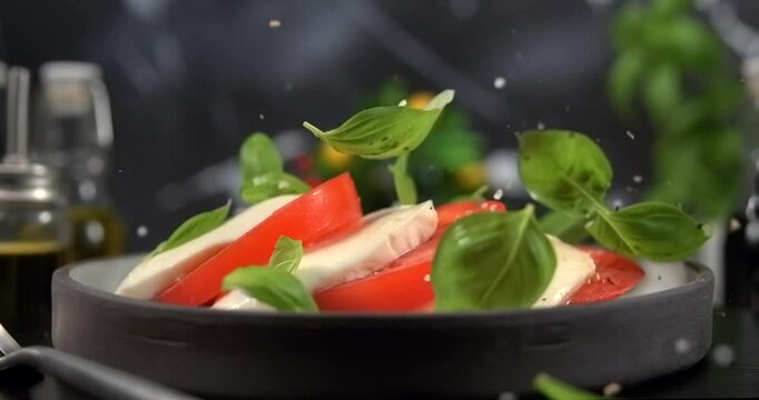 Basil leaves falling onto caprese salad on black background slow motion 1000 fps