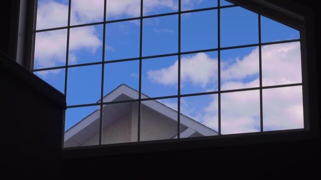 Time-lapse video of blue sky and clouds moving by from the transom window of the interior of a house.