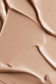 Beige cosmetic foundation or makeup product creating a textured swatch, showing creamy consistency and fluid spreading
