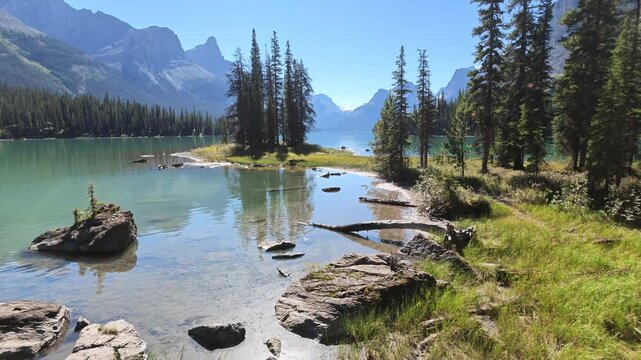 Spirit Island with evergreen trees on a rocky peninsula in turquoise glacial waters of Maligne Lake, framed by towering Rocky Mountain peaks under blue sky in Jasper National Park in Alberta of Canada