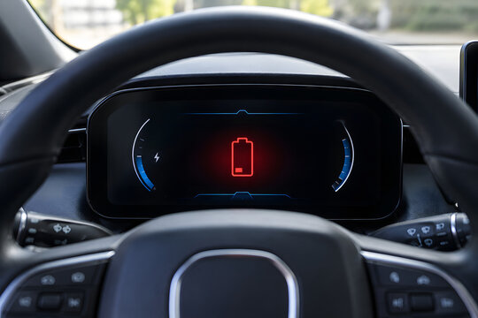 Digital car dashboard displays a red battery warning icon behind the steering wheel, indicating an electrical system alert, charging fault concept, vehicle diagnostics, maintenance, and repair.