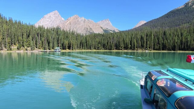 Tour boat cruising on Maligne Lake with Spirit Island, surrounded by dense evergreen forests and towering Rocky Mountains on a sunny summer day in Alberta, Canada in Jasper National Park