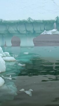Vertical Video of Floating Ice Fragments on Blue-Green Water. Broken white ice spreads across blue-green water, showing varied frozen shapes, surface texture and gentle ripples in a natural seascape.