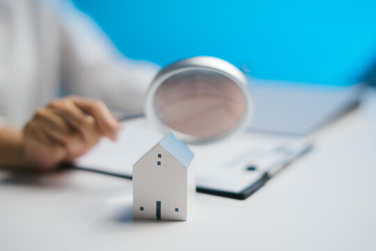 Focused professional analyzing home model with magnifying glass for real estate inspection, feeling curious and attentive