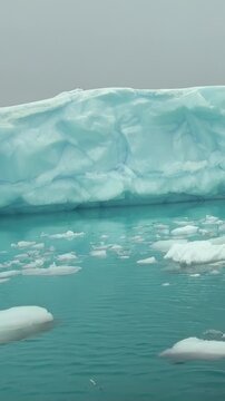 Vertical Video of Floating Ice Fragments Scattered Across Open Water. Broken white ice spreads across blue-green water, showing varied frozen shapes, texture and gentle ripples.