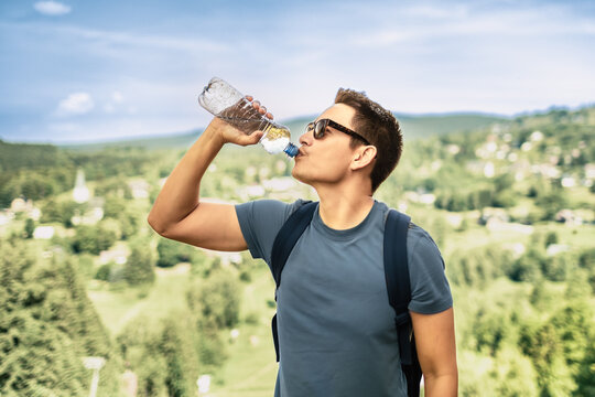 Male hiker drinking water from a bottle outdoors during summer hike with scenic mountain landscape