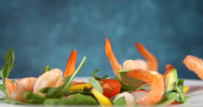 Shrimp falling onto fresh vegetable salad with avocado in slow motion