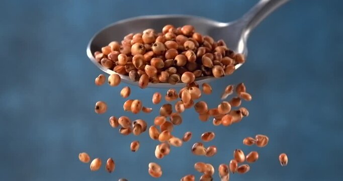 Sorghum grains falling from spoon in slow motion on blue background