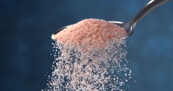Pink Himalayan salt falling from spoon in slow motion on blue background