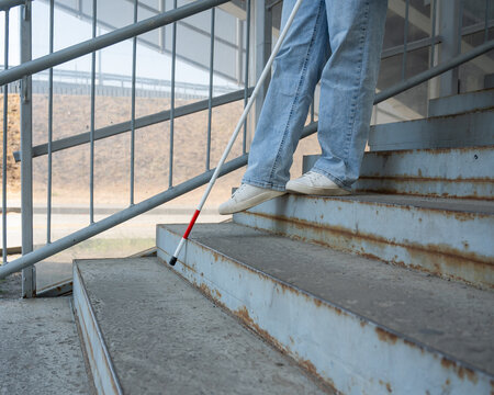 A blind woman descends a staircase. Close-up of her feet and a tactile stick.