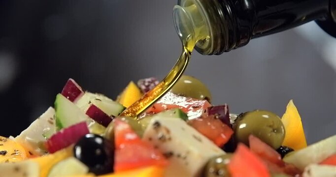 Olive oil pouring onto fresh greek salad with feta cheese olives tomato and cucumber in slow motion