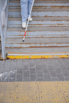 A blind woman descends a staircase. Close-up of her feet and a tactile stick.