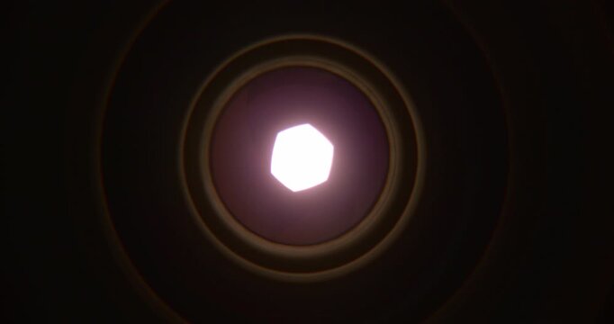 Extreme closeup of a camera lens aperture slowly opening as intense bright light emerges from behind the blades. Cinematic visual representing photography, optics, focus, exposure, illumination.