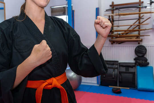 Woman wearing a black dobok and orange belt, practicing hapkido in a dojo, showing a fighting stance