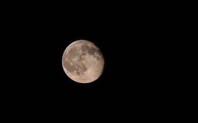 Fototapeta premium Clear telephoto shot of the full moon shining brightly in a pitch-black night sky, highlighting detailed lunar surface, craters, and maria.